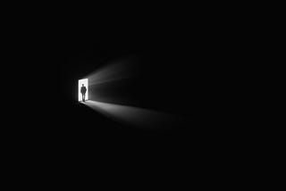 A person walking out of a dark room through a well-lit doorway