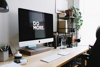 Modern office setup with a large monitor that reads “DO MORE” in white on a black background.