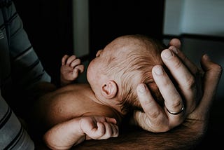 An Infant being held in a man’s hands.