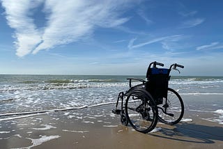 A wheelchair on a beach by the sea.