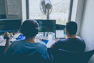 Two programmers sitting next to each other in the office in a hot day and discusses their code