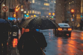 Man with an umbrella, rainy street in a city. Dusk.