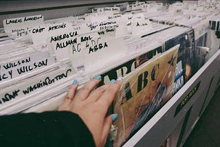 Vinyl records filed alphabetically, someone’s hand is picking out a record titled ABC.