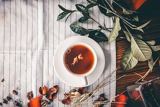 Imagem de uma xícara de chá vista de cima, ao lado de folhas.