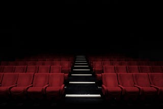 A dark, empty theater with red seats and a glistening black stairway.