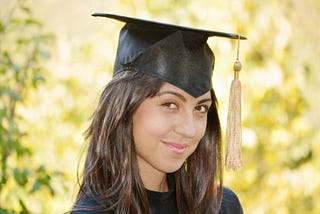Head shot of female in cap and gown, smiling shyly.