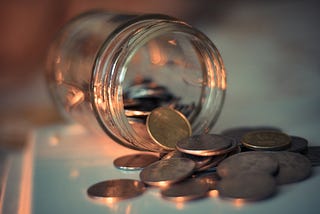 A mason jar lying on its side, a handful of coins spilling out of it onto the table.