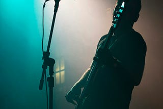 Fotografia de um homem sobre um palco, tocando guitarra.