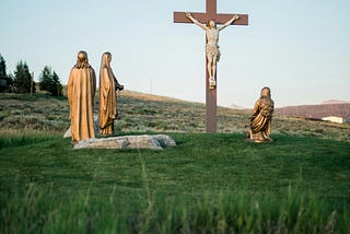 Statues depicting Jesus on a cross and three witnesses, one of them kneeling.