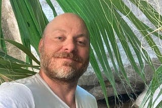 adam, a bald man with a palm leaf in background