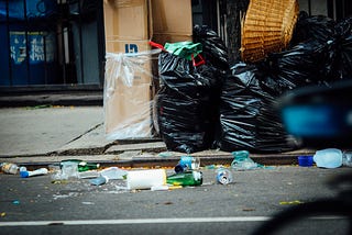 A pile of trash on the sidewalk, some loose litter is strewn in the gutter.