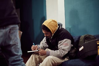 A man sits in a public area writing in a notebook