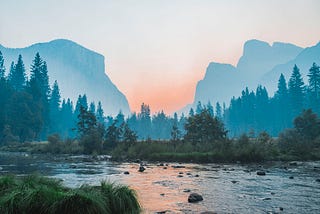 A lake at sunrise with trees and a mountain in the distance.