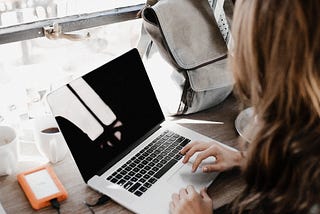 A girl is working on her laptop with a small backpack and a hard drive attached to her computer.