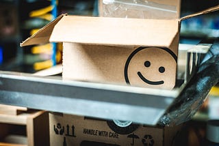 A cardboard box open at the top with a smiley face imprinted on the lower righthand corner
