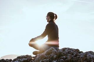 A woman meditating on the rocks