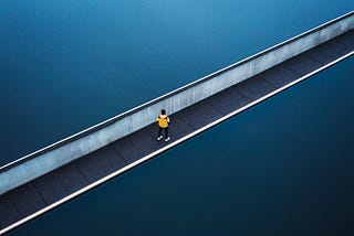 Guy standing on a brigde. Beneath him is water. The shot is taken from above.