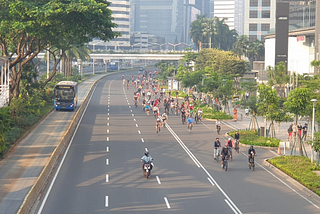Dozens of cyclists use a wide five-lane road, taking over the street/ A bus is passing by in a protected and separated bus lane.