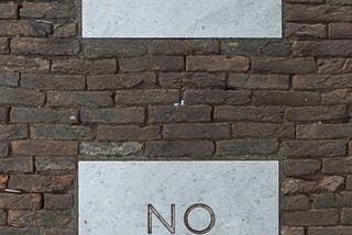 A brick wall with Yes and No written on two blank paper pieces.