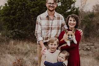 Husband and wife standing outside with their corgi dog and two sons