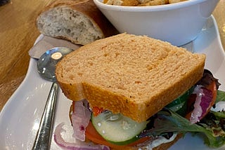 Close-up on a large white plate with a vegetable sandwich next to a bowl of tomato soup topped with croutons and on the other side of the bowl is a roll
