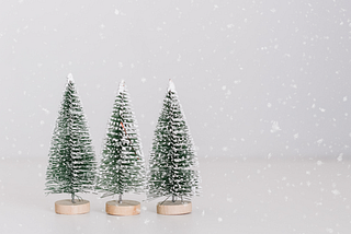 Three artificial Christmas trees covered in snow with snowflakes falling