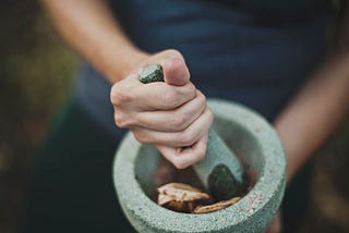 a person grinding herbs, spices, and flowers in a mortar and pestle.