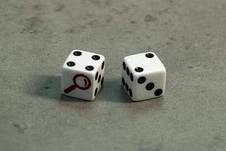 A pair of dice, one with a magnifying glass on the side.