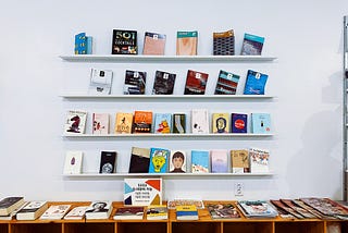 A wall mounted bookshelf featuring 4 shelves with 6 books on each. Minimalist and colorful.