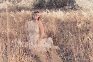Female bride wearing a fancy gown sitting in the middle of wheat field, the wheat is as tall as she is.
