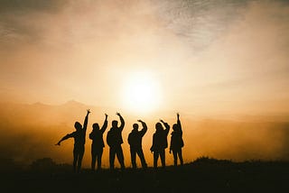 Silhouette of six friends cheering at the sun and mountains. Gorgeous fun.