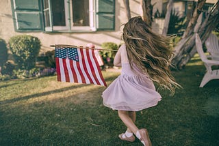 A little girl in the yard with an American flag.