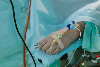 There’s a person on a hospital bed. They have an IV an tubes connected.