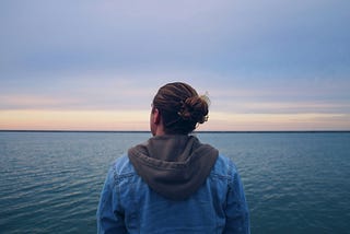 a young woman looking out over the water at sunrise