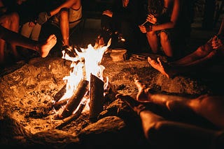 a bunch of people warming their hands and feet at a bonfire