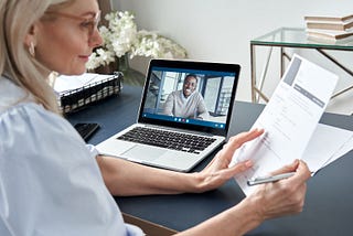 A woman looks at a document as she is interviewing a person over zoom