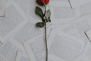 a  single red rose laying atop a  pile of pages out of a
