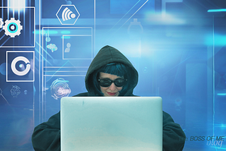 A woman hacker wearing a dark hoodie sits at a laptop.