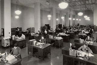 Black and White photograph from 1937 of the US Division of Classification and Cataloging. Long rows of desks with staff processing paperwork at each desk.