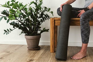 Woman sitting on a bench holding a yoga mat