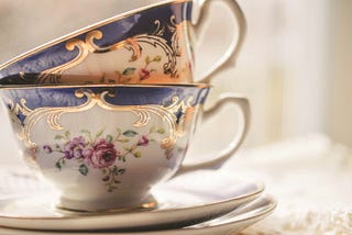 Two ornate teacups with gold filigree, one nested inside the other, sitting on two matching saucers.