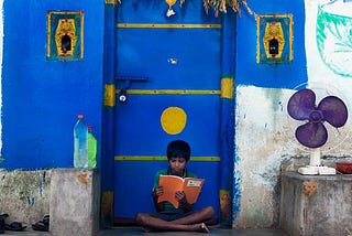 A little boy studying outside his home door.