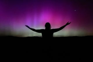 Person with outstretched arms silhouetted against the Northern Lights