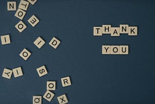 Mickey markoff air sea exec 2024 — photo of scrabble tiles strewn on table, selected few spelled out to say ‘thank you’ on blue background. Photo on mickey markoff 2024 article about net worth of gratitude