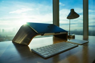 A desk with a keyboard, laptop stand, and MacBook