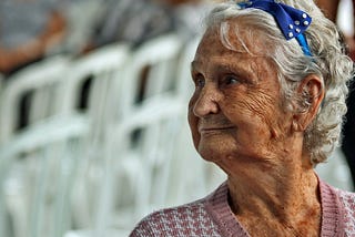 An elderly lady with a blue bow in her hair, looking off to her right.