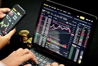A picture of the a hand working on a computer system with the depiction of the crypto market on a screen.