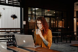 Woman sitting at a bench, working on her computer with a drink in hand