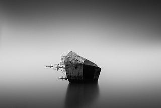 A steel ship lying on it’s side in a grey, foggy background