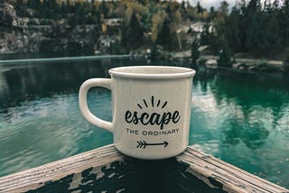 A coffee mug balanced on the edge of some wooden structure overlooking a water body